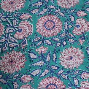 May include: Teal fabric featuring a repeating floral design. Large pink and white flowers with blue centres and stems are spread across the surface. The leaves are blue and white, creating a vibrant, detailed pattern.