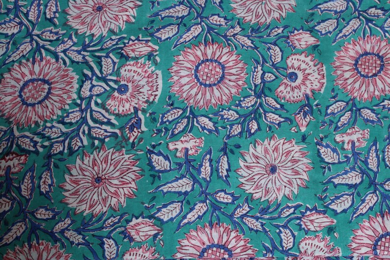 May include: Teal fabric featuring a repeating floral design. Large pink and white flowers with blue centres and stems are spread across the surface. The leaves are blue and white, creating a vibrant, detailed pattern.