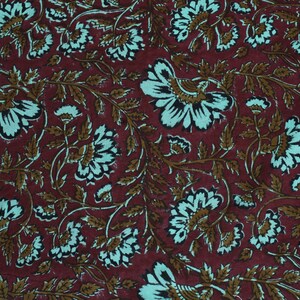 May include: Burgundy fabric with a repeating floral pattern. The design features large white and teal flowers with brown stems and leaves. The fabric has a textured appearance, suitable for various craft projects or home decor.