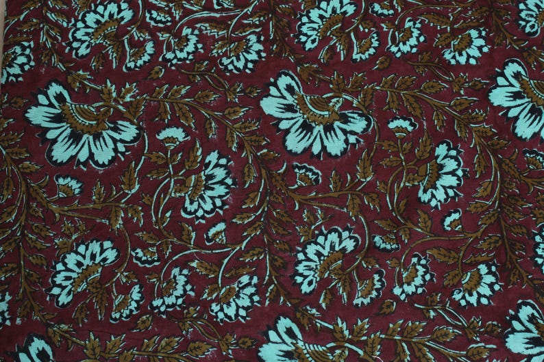 May include: Burgundy fabric with a repeating floral pattern. The design features large white and teal flowers with brown stems and leaves. The fabric has a textured appearance, suitable for various craft projects or home decor.