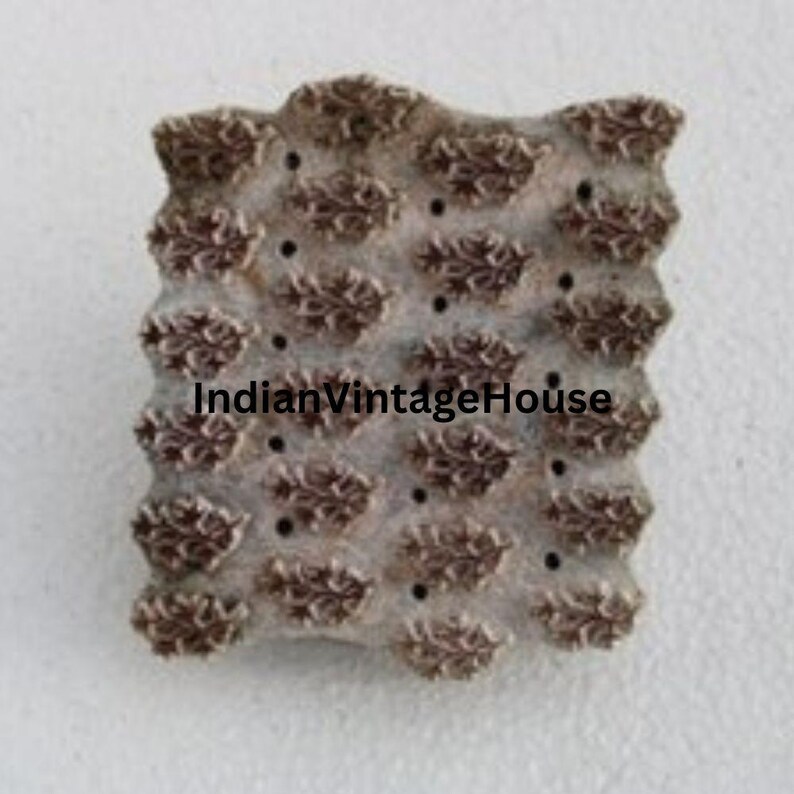 May include: A wooden block printing stamp with a repeating pattern of floral designs. The stamp is brown and has a textured surface. The text "IndianVintageHouse" is printed on the stamp.