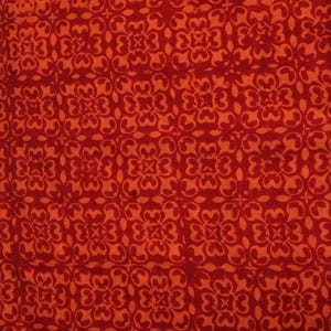 May include: Close-up of a fabric with a repeating floral pattern in shades of red and orange. The design features stylized flowers arranged in a grid-like formation, creating a textured and visually engaging surface.