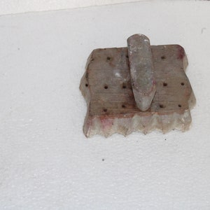 May include: A wooden mold with a handle, used for making cookies or other pastries. The mold has a scalloped edge and a series of holes in the surface.