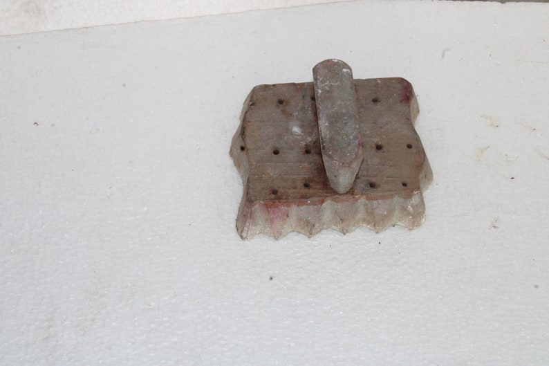 May include: A wooden mold with a handle, used for making cookies or other pastries. The mold has a scalloped edge and a series of holes in the surface.
