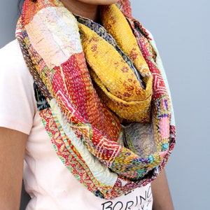 May include: A colourful patchwork scarf made from recycled saris. The scarf is a mix of red, yellow, blue, and green fabrics with intricate embroidery. It is a unique and stylish accessory.