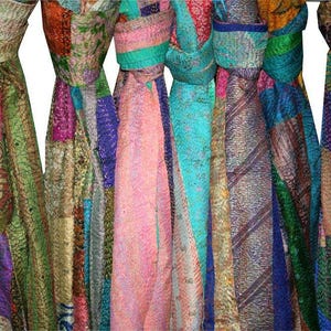 May include: A collection of colorful, patchwork scarves hanging against a white background. The scarves feature a variety of patterns and colors, including pink, green, purple, and blue. The scarves appear to be made of a soft, lightweight fabric.