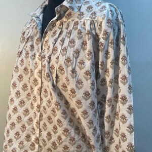 May include: A white shirt with a brown and olive floral print. The shirt features a classic collar and long sleeves. The garment is displayed on a mannequin.