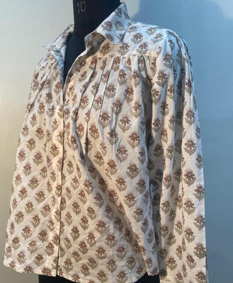 May include: A white shirt with a brown and olive floral print. The shirt features a classic collar and long sleeves. The garment is displayed on a mannequin.