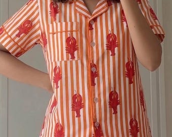 May include: Orange and white striped pajama set with a red lobster pattern. The short-sleeved shirt has a front pocket and button closure. The shorts have a matching lobster print.