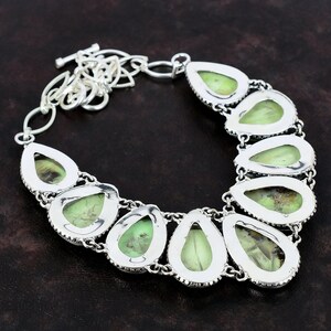 May include: A silver necklace featuring a teardrop-shaped green gemstone pendant. The necklace has a silver chain and a clasp.