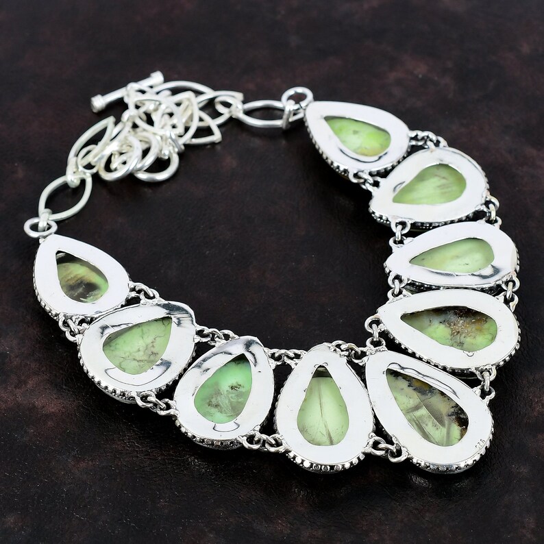 May include: A silver necklace featuring a teardrop-shaped green gemstone pendant. The necklace has a silver chain and a clasp.