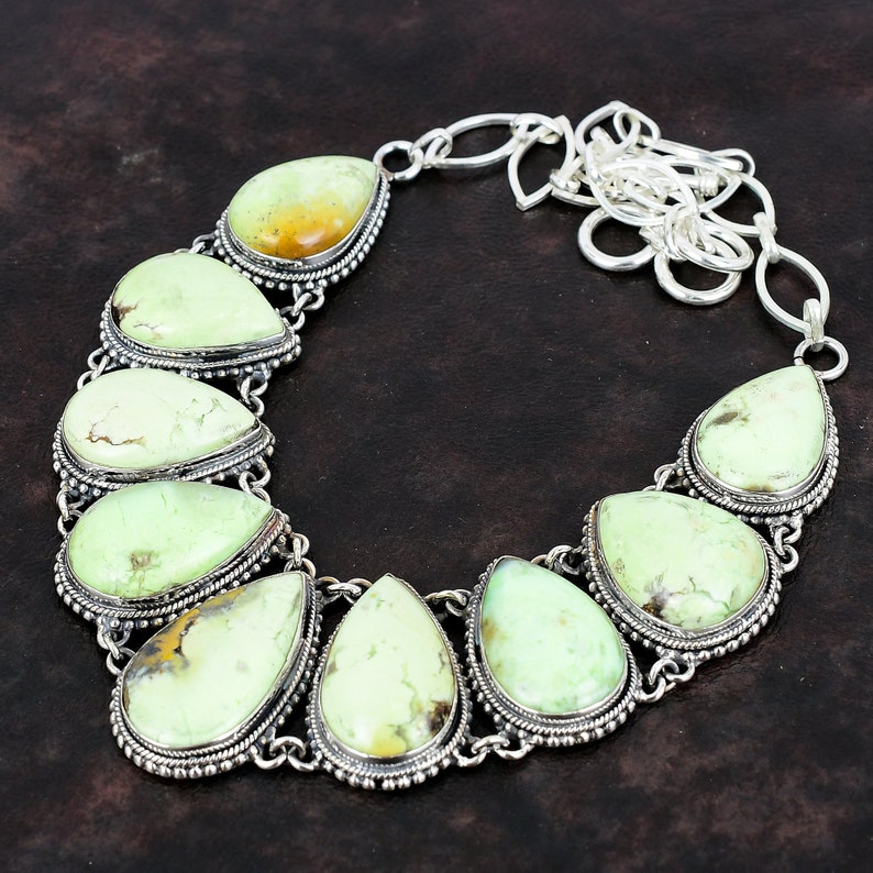 May include: A silver necklace featuring a chain and seven teardrop-shaped green gemstones. The gemstones are set in silver bezels with decorative borders.