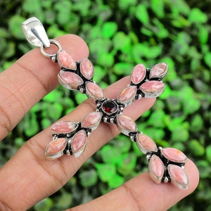 May include: A silver cross pendant with a red gemstone in the centre and pink stones around it.