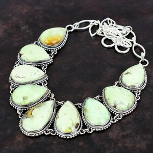 May include: A silver necklace featuring a chain and seven teardrop-shaped green gemstones. The gemstones are set in silver bezels with decorative borders.