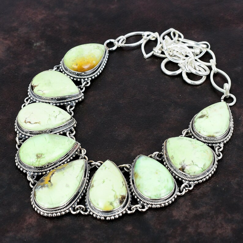May include: A silver necklace featuring a chain and seven teardrop-shaped green gemstones. The gemstones are set in silver bezels with decorative borders.