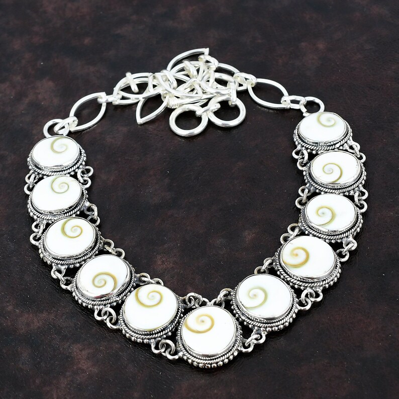 May include: A silver necklace with a chain and a pendant made of white shell with a brown spiral pattern.