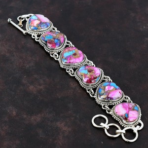 May include: A silver bracelet with a heart-shaped design. The hearts are made of pink, blue, and white stone. The bracelet has a toggle clasp.