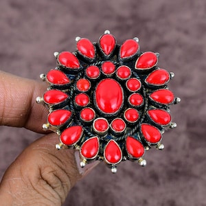 Könnte beinhalten: Ein silberner Ring mit einem großen roten Korallenstein in der Mitte, umgeben von kleineren roten Korallensteinen. Der Ring hat ein florales Design.