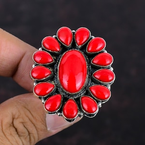 May include: A silver ring with a large red coral stone in the center and smaller red coral stones surrounding it.