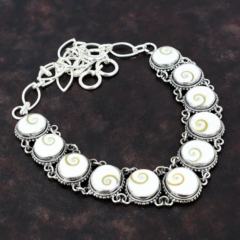May include: A silver necklace with a chain and eight round white and brown abalone shell pendants. Each pendant is surrounded by a silver border.