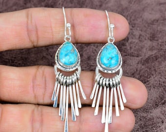 May include: A pair of silver earrings with turquoise teardrop-shaped stones. The earrings have a fringe design with multiple silver bars hanging from the bottom. The turquoise stones are a bright, vibrant blue.