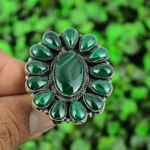 May include: A silver ring featuring a large oval green malachite stone surrounded by smaller green malachite stones.
