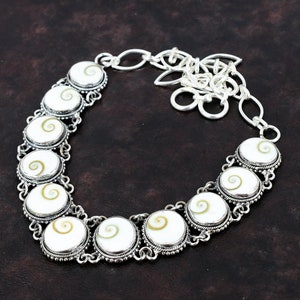 May include: A silver necklace with a chain and a series of round white and brown shell pendants. The pendants have a spiral pattern.