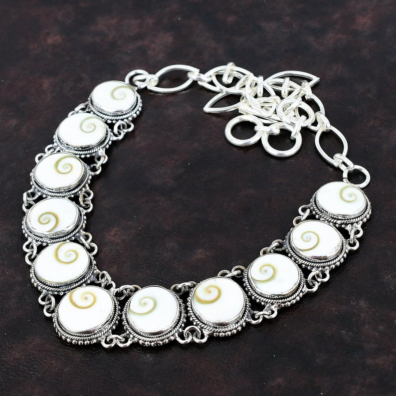 May include: A silver necklace with a chain and a series of round white and brown shell pendants. The pendants have a spiral pattern.