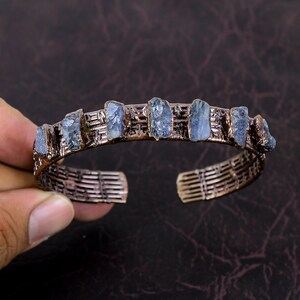 May include: A copper wire bracelet with a woven design and blue gemstone accents.