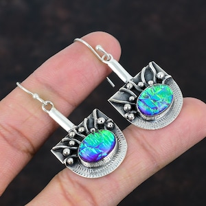 Pode incluir: Um par de brincos de prata com uma pedra verde e azul iridescente engastada em uma moldura de prata. A moldura tem um design decorativo com pequenas contas de prata.