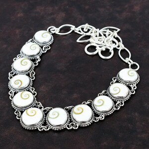 May include: A silver necklace with a chain and a series of round white and brown shell pendants. The pendants have a spiral pattern.