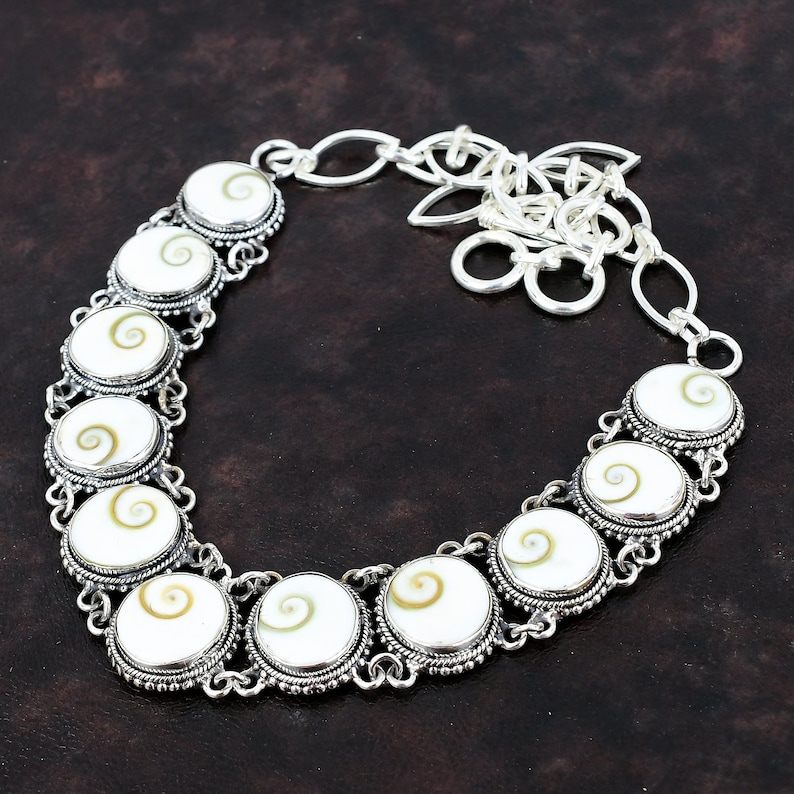 May include: A silver necklace with a chain and a series of round white and brown shell pendants. The pendants have a spiral pattern.