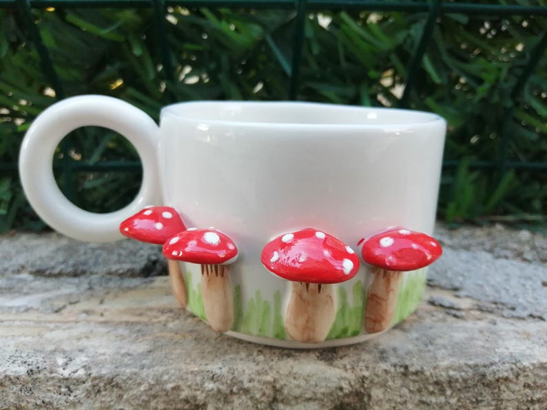 May include: White ceramic mug with a handle and four red and white mushrooms attached to the side.