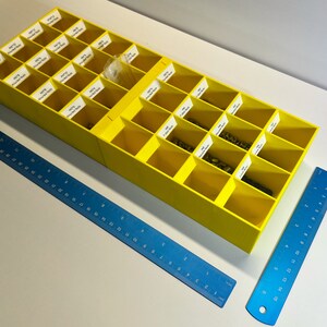 Könnte beinhalten: Eine gelbe Plastik-Aufbewahrungsbox mit 24 Fächern, die jeweils mit einer Nummer und den Worten "Rounded Ends" beschriftet sind. Die Box ist geöffnet und enthält kleine Metallteile.
