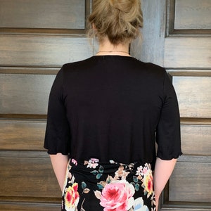 Puede incluir: Una blusa negra de manga corta con una falda de estampado floral. La blusa tiene un escote redondo y la falda tiene una cintura alta.