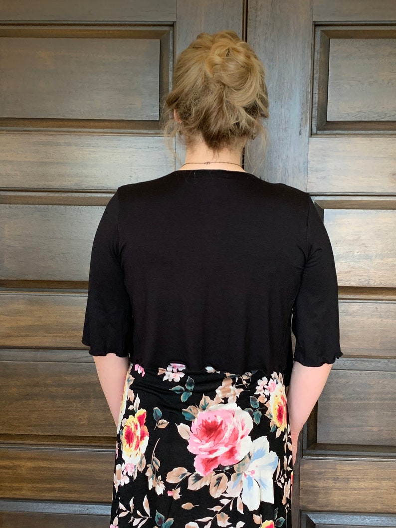 Puede incluir: Una blusa negra de manga corta con una falda de estampado floral. La blusa tiene un escote redondo y la falda tiene una cintura alta.