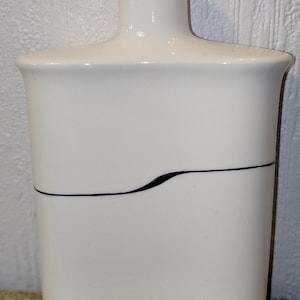 以下が含まれることがあります： 黒い波状の線模様が施された白いセラミックボトル。ボトルは丸みを帯びた、わずかに広がったトップを持っています。