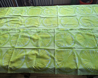 May include: Two green fabric placemats with a white geometric pattern of circles with radiating lines. The placemats are folded in half and have a light green background.