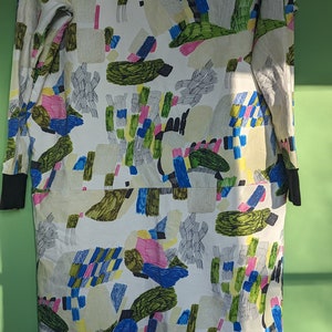 Könnte beinhalten: Ein weißes, langärmeliges Kleid mit einem abstrakten Muster in Grün-, Blau-, Rosa- und Gelbtönen.