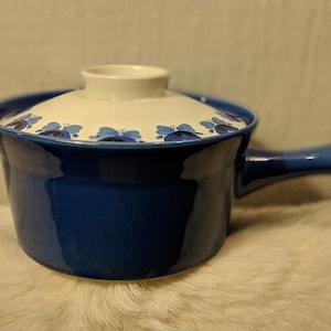 以下が含まれることがあります： 白い蓋と青い取っ手がついた青いセラミック製の食器。蓋は白い背景に青い花柄が描かれています。