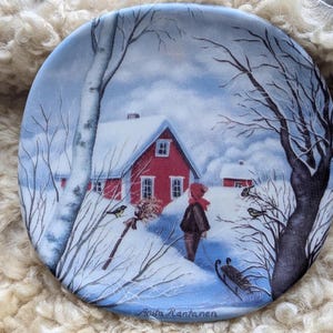 Pode incluir: Uma cena de inverno com uma casa vermelha, árvores cobertas de neve e uma pessoa caminhando na neve. O texto "Anita Rantanen" está na parte inferior da imagem.