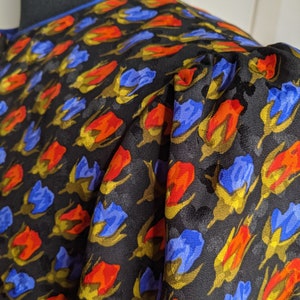 May include: Black fabric with a repeating pattern of blue, orange, and yellow stylized flowers.