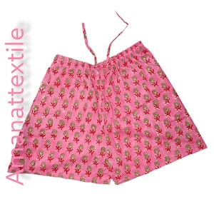 Puede incluir: Shorts rosas con un estampado floral en rojo y dorado. Los shorts tienen cintura con cordón. El texto "Annattextile" está impreso verticalmente en el lado izquierdo.