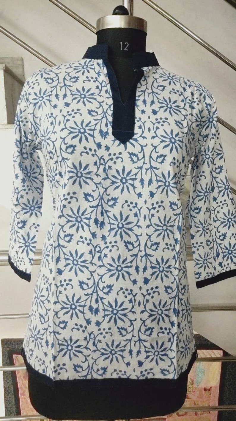 May include: White cotton tunic top with a blue floral print and a dark blue trim around the neckline and hem.
