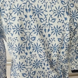 May include: A white cotton tunic with a blue floral print and a navy blue collar.