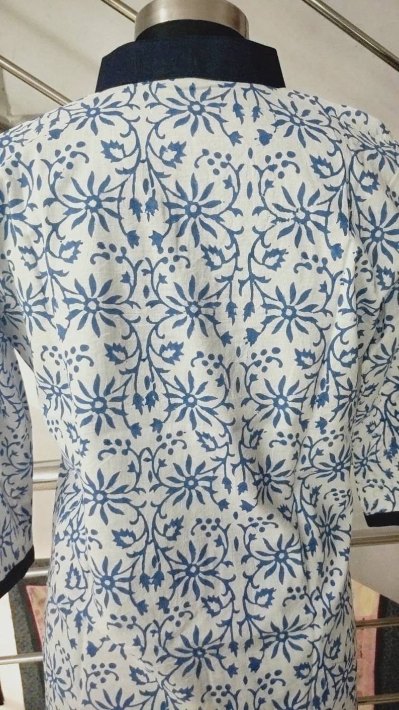May include: A white cotton tunic with a blue floral print and a navy blue collar.
