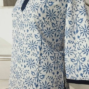 May include: A white cotton tunic with a blue floral print and a black trim. The tunic has a mandarin collar and three-quarter sleeves.