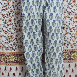 May include: White cotton pants with a blue and green floral print. The pants have a drawstring waist and a wide leg.