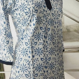 May include: A white cotton top with a blue floral print and a dark blue trim around the neckline and hem.