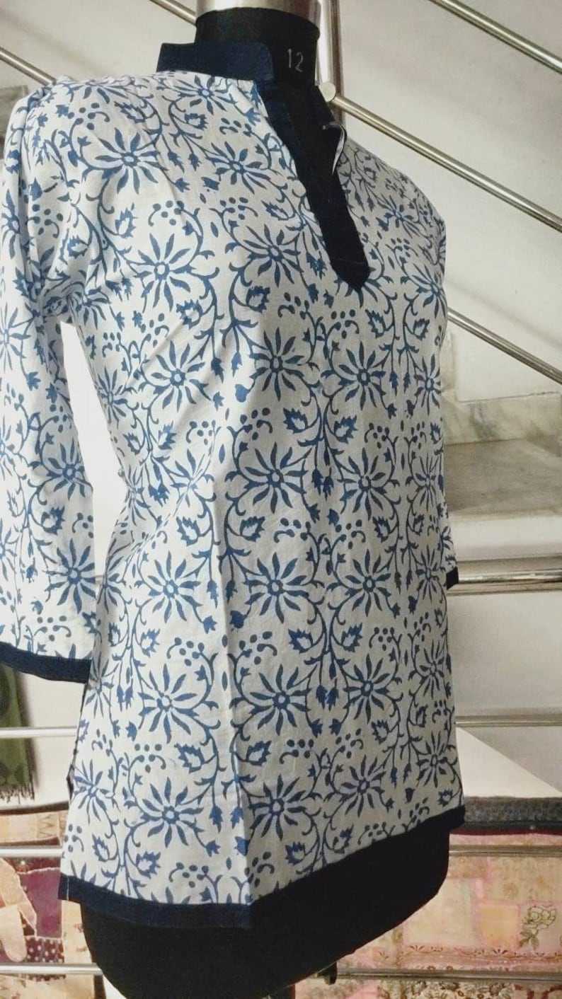 May include: A white cotton top with a blue floral print and a dark blue trim around the neckline and hem.